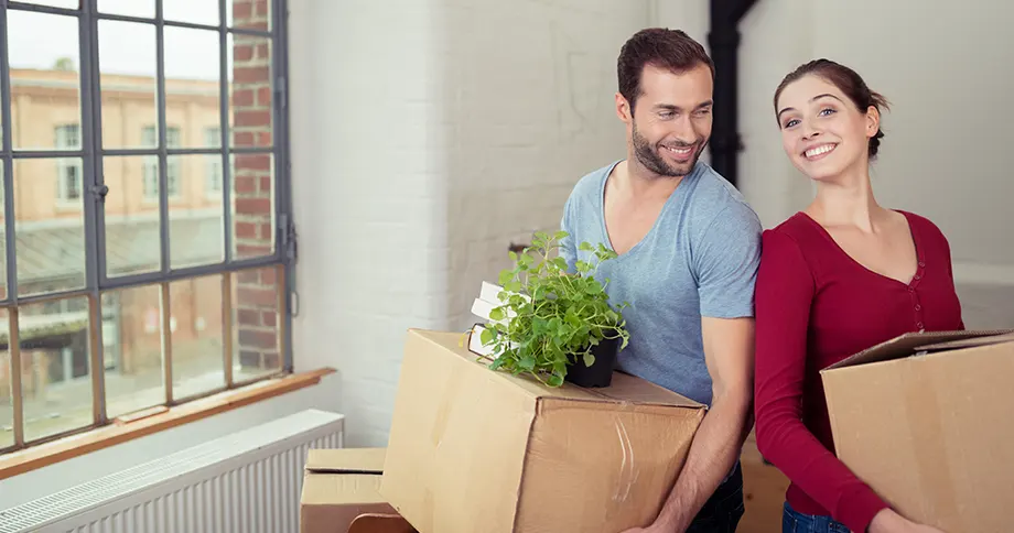 Pärchen mit Umzugskartons in der Hand freut sich über den Einzug in die neue Wohnung