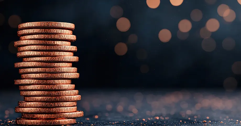 Ein gleichmäßiger Stapel glänzender Kupfermünzen auf dunkler, glitzernder Oberfläche. Es repräsentiert die transparenten Preise der KI-Funktionen in immoprofessional.